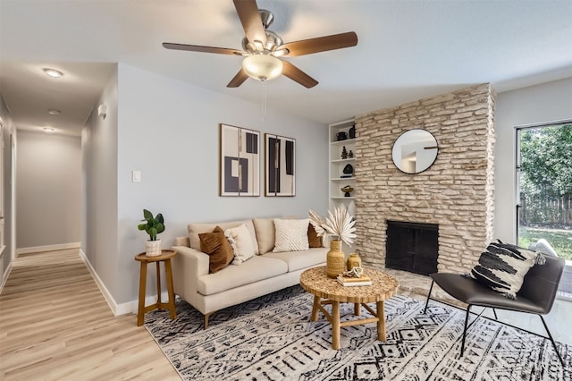 living room featuring built in features, light hardwood / wood-style floors, a stone fireplace, and plenty of natural light