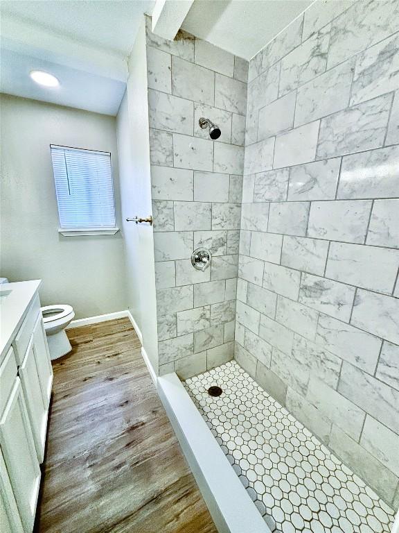 bathroom with tiled shower, toilet, baseboards, wood finished floors, and vanity