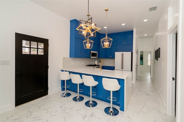 kitchen featuring hanging light fixtures, light tile patterned floors, white fridge, blue cabinets, and backsplash