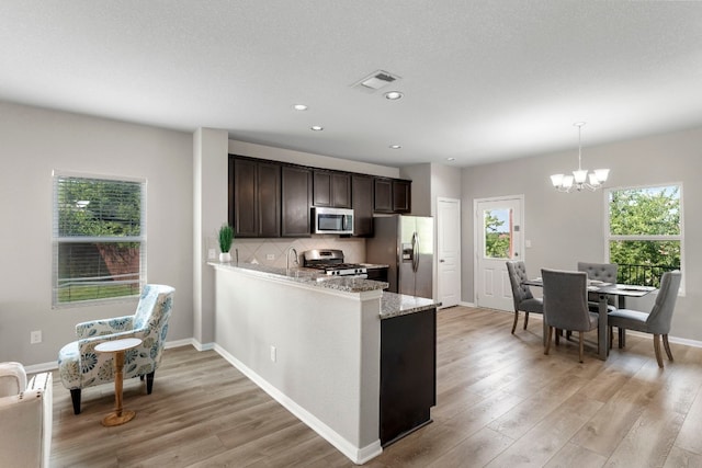 kitchen featuring pendant lighting, appliances with stainless steel finishes, backsplash, dark brown cabinets, and light stone countertops