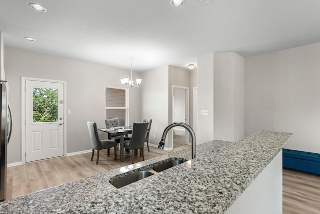 kitchen featuring pendant lighting, light hardwood / wood-style floors, light stone countertops, and sink