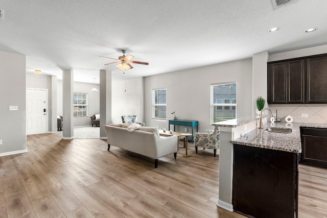 living room featuring ceiling fan, sink, a textured ceiling, and light wood-type flooring