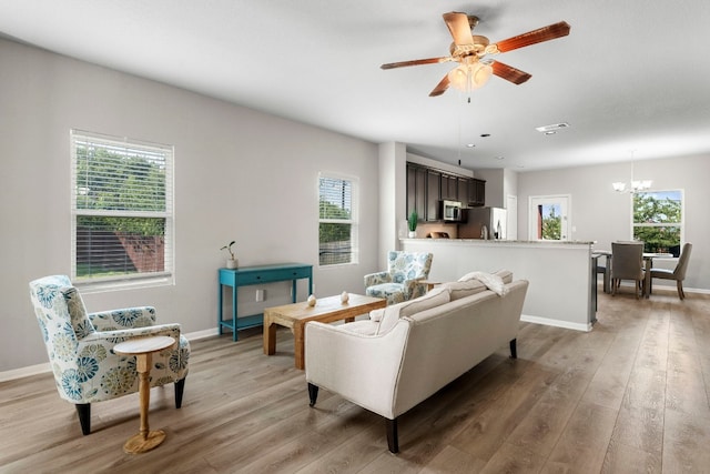 living room with ceiling fan with notable chandelier and light hardwood / wood-style floors