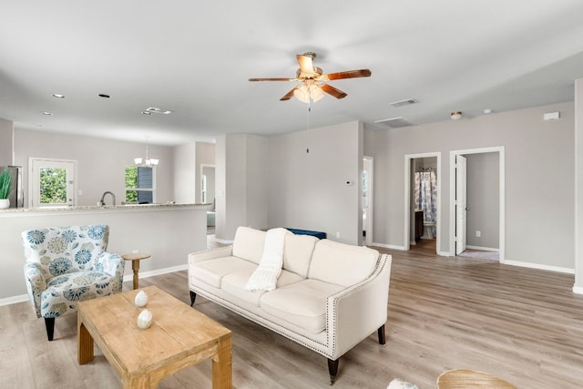 living room with ceiling fan with notable chandelier and light hardwood / wood-style flooring