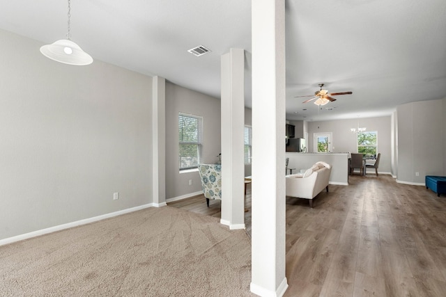 unfurnished living room featuring ceiling fan with notable chandelier, light carpet, and a wealth of natural light