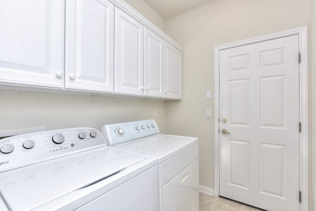 clothes washing area with light tile patterned flooring, washing machine and dryer, and cabinets