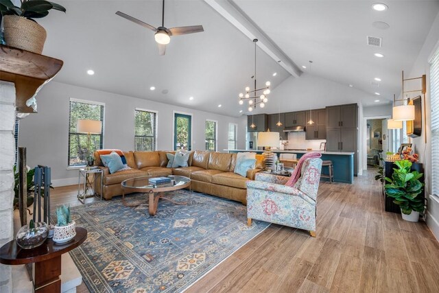 living room featuring light wood-type flooring, high vaulted ceiling, ceiling fan with notable chandelier, a fireplace, and beam ceiling