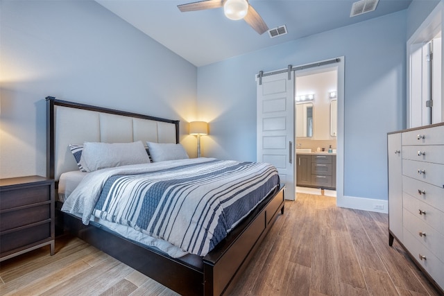 bedroom with ceiling fan, a barn door, light hardwood / wood-style flooring, and ensuite bath