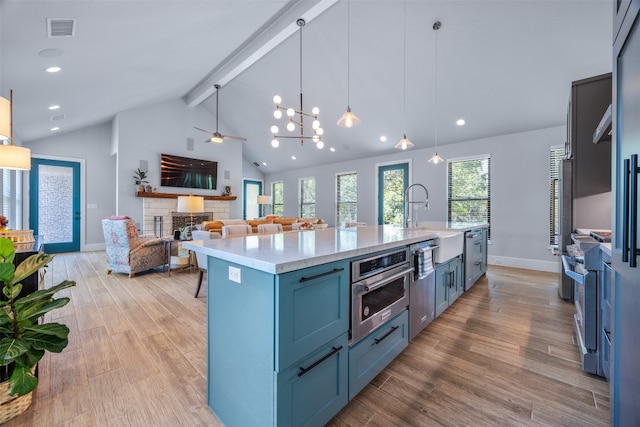 kitchen featuring pendant lighting, a kitchen island with sink, appliances with stainless steel finishes, light wood-type flooring, and beam ceiling