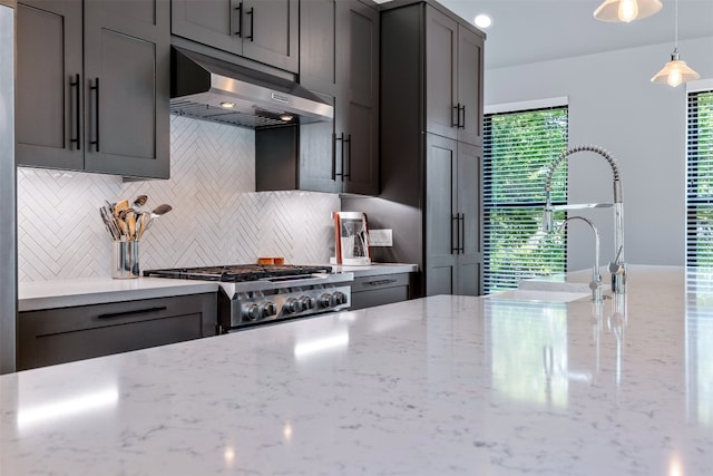 kitchen with stove, light stone counters, wall chimney exhaust hood, and decorative backsplash