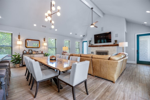 dining room with ceiling fan with notable chandelier, high vaulted ceiling, light hardwood / wood-style floors, a fireplace, and beamed ceiling