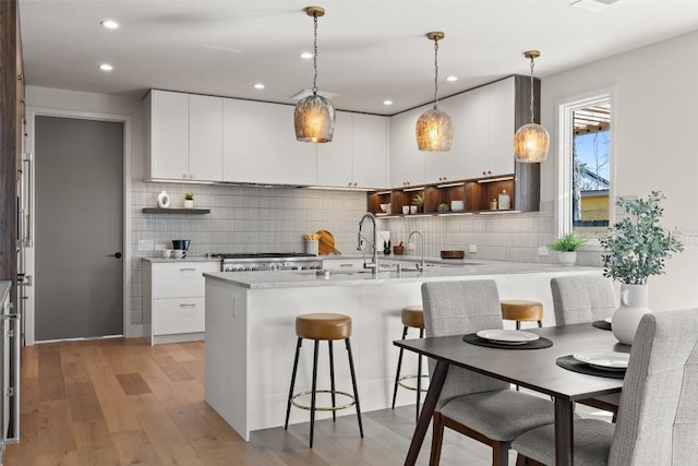 kitchen featuring white cabinetry, backsplash, hanging light fixtures, and light hardwood / wood-style flooring