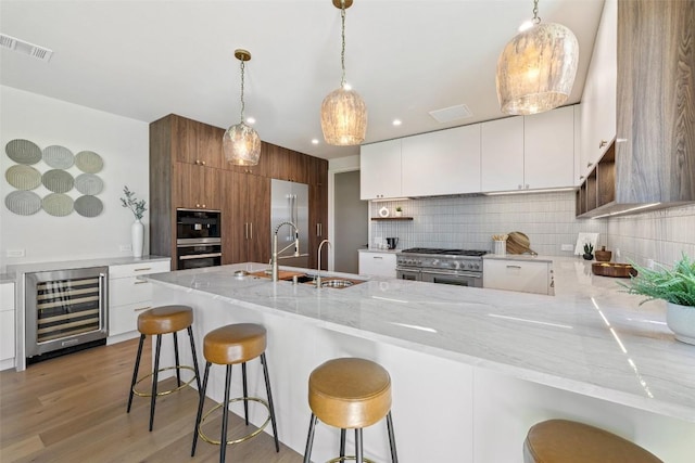 kitchen with premium appliances, beverage cooler, sink, white cabinets, and a breakfast bar area