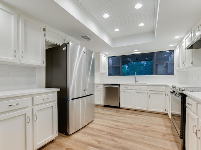 kitchen featuring a raised ceiling, light wood-type flooring, stainless steel appliances, backsplash, and white cabinets