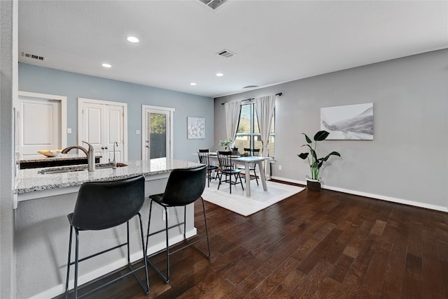 kitchen with dark wood-type flooring, a breakfast bar area, sink, and light stone counters