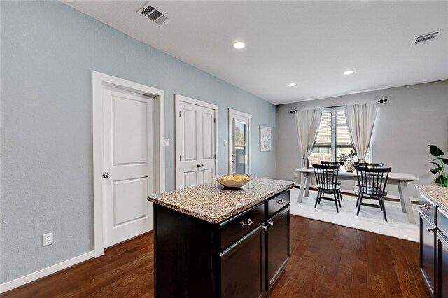 kitchen with a kitchen island, dark brown cabinets, dark hardwood / wood-style floors, and light stone counters