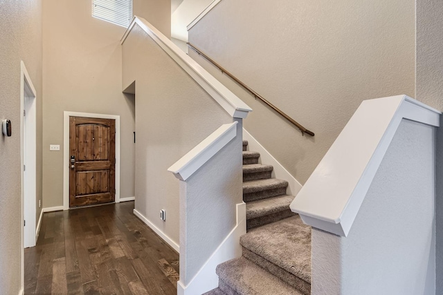 stairway with hardwood / wood-style floors and a towering ceiling