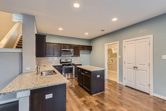 kitchen featuring sink, light stone countertops, hardwood / wood-style floors, a center island, and stainless steel appliances