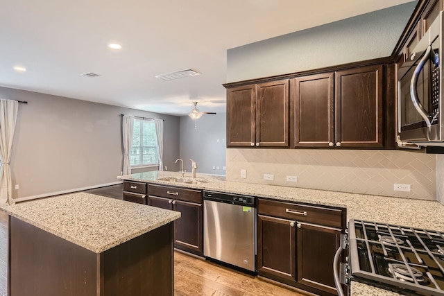 kitchen with dark brown cabinetry, light stone counters, light hardwood / wood-style flooring, and appliances with stainless steel finishes