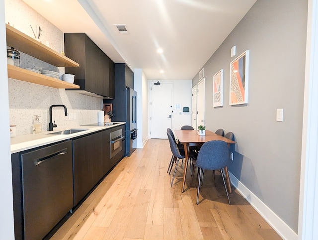 kitchen with dark brown cabinets, light hardwood / wood-style floors, backsplash, stainless steel appliances, and sink