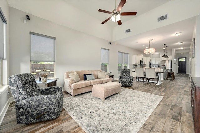 living room featuring ceiling fan with notable chandelier, vaulted ceiling, and dark wood-type flooring