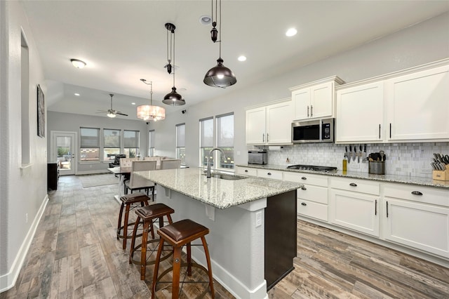 kitchen featuring sink, stainless steel appliances, decorative light fixtures, a center island with sink, and white cabinets