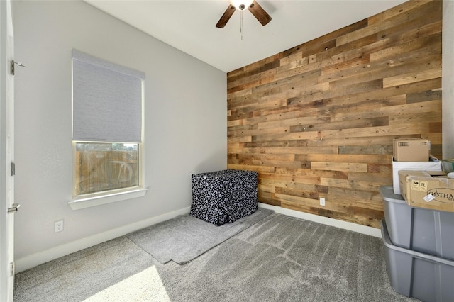 living area featuring carpet flooring, ceiling fan, and wood walls