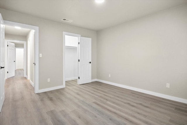 unfurnished bedroom featuring a spacious closet, a closet, and light hardwood / wood-style floors