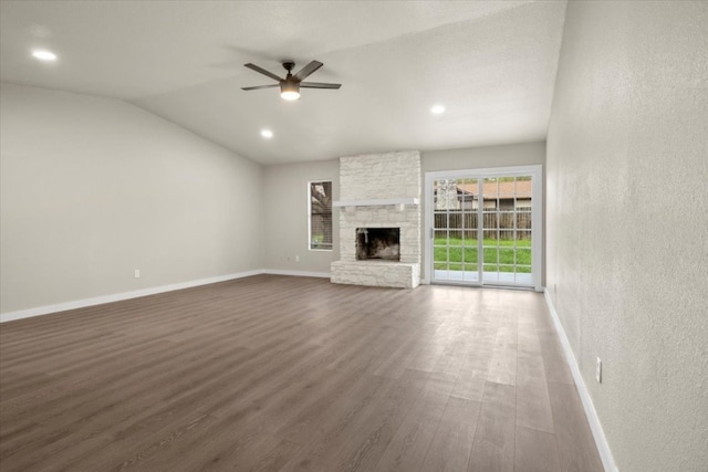 unfurnished living room featuring ceiling fan, wood-type flooring, lofted ceiling, and a stone fireplace