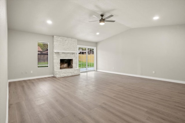 unfurnished living room with ceiling fan, wood-type flooring, a stone fireplace, and lofted ceiling