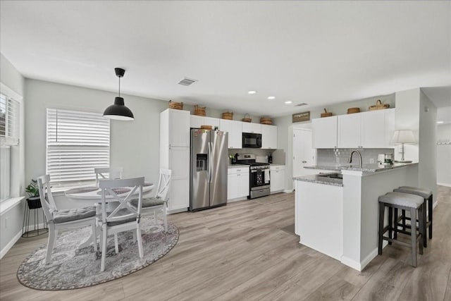 kitchen featuring appliances with stainless steel finishes, decorative light fixtures, white cabinetry, light stone counters, and kitchen peninsula