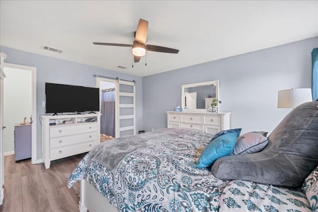 bedroom with ceiling fan, a barn door, and light hardwood / wood-style floors