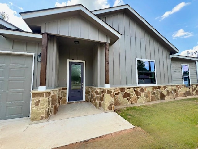 entrance to property with an attached garage, stone siding, board and batten siding, and a yard