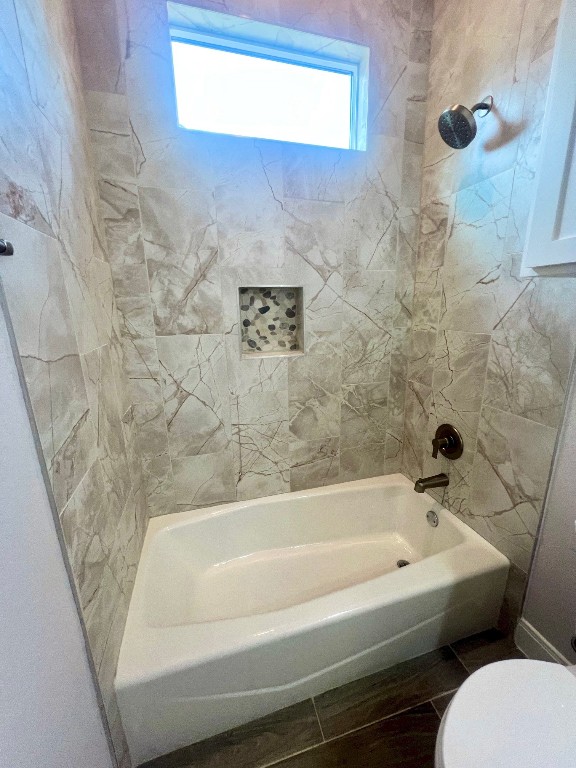 bathroom with toilet, tile patterned flooring, and tiled shower / bath