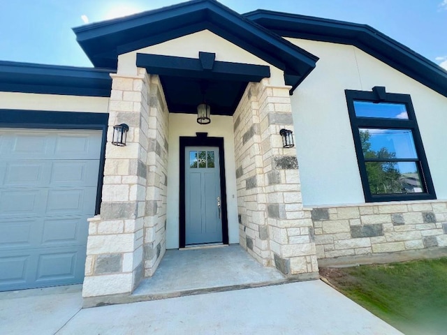 doorway to property with stone siding, an attached garage, and stucco siding