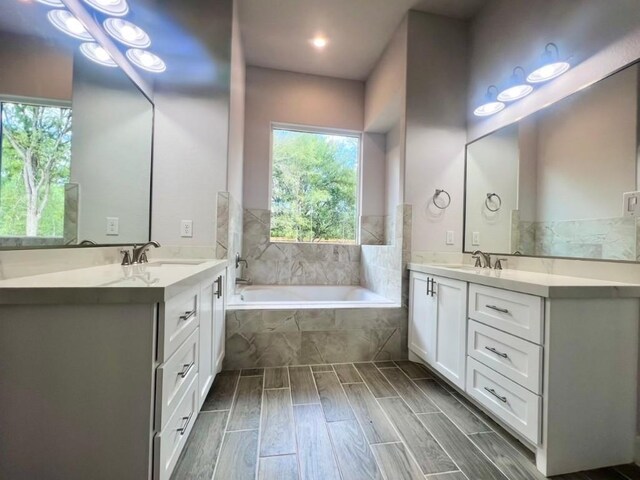 bathroom with tiled tub, vanity, and wood-type flooring