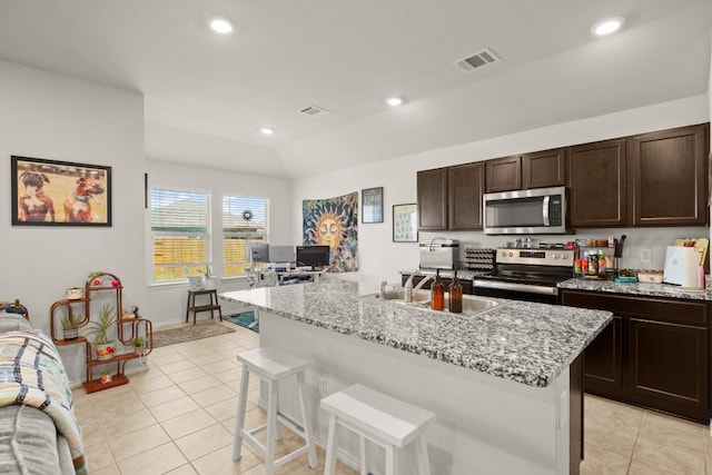 kitchen with light tile patterned floors, appliances with stainless steel finishes, light stone countertops, a center island with sink, and sink