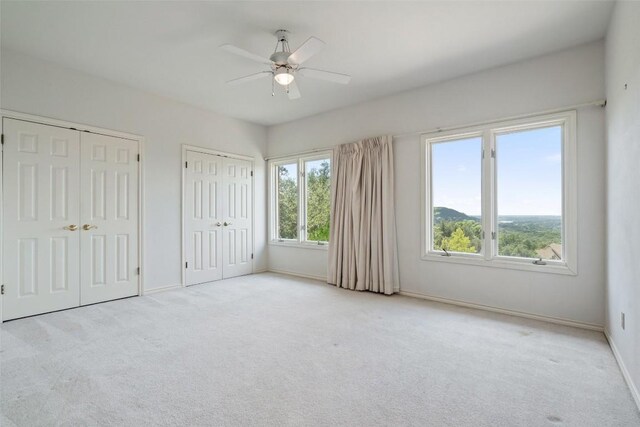 unfurnished bedroom featuring light colored carpet, ceiling fan, and two closets