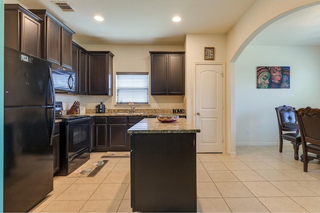 kitchen with black appliances, light tile patterned flooring, a center island, and dark brown cabinetry