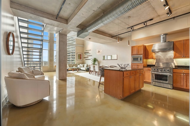 kitchen with wall chimney range hood, a towering ceiling, stainless steel appliances, a kitchen breakfast bar, and a kitchen island