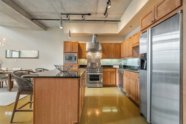 kitchen featuring appliances with stainless steel finishes, a kitchen bar, track lighting, a kitchen island, and wall chimney exhaust hood