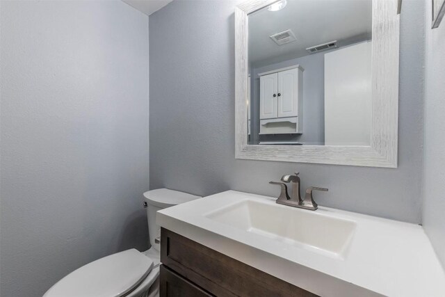 bathroom featuring vanity, toilet, a textured wall, and visible vents