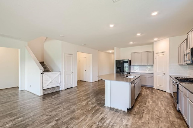 kitchen featuring hardwood / wood-style flooring, gray cabinetry, stainless steel appliances, an island with sink, and sink