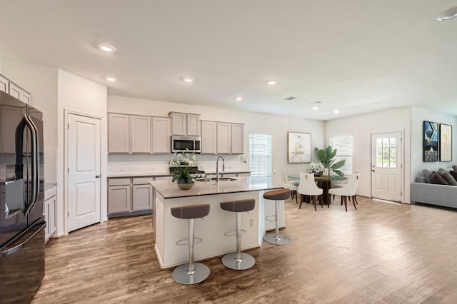 kitchen with gray cabinetry, a kitchen breakfast bar, black refrigerator, sink, and a kitchen island with sink