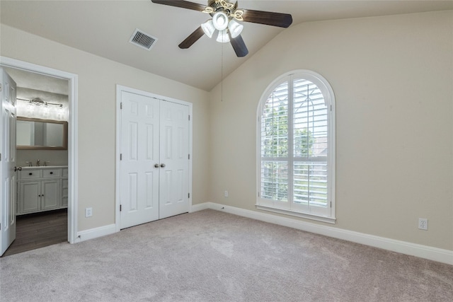 unfurnished bedroom featuring ceiling fan, ensuite bath, light carpet, and vaulted ceiling