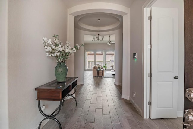 corridor featuring a tray ceiling and a notable chandelier