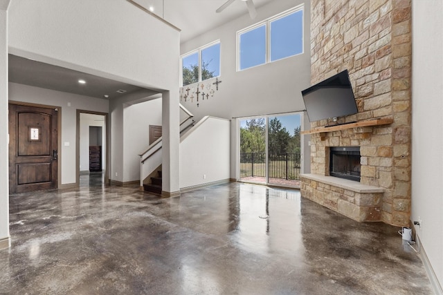 unfurnished living room featuring ceiling fan, concrete flooring, a stone fireplace, and a wealth of natural light