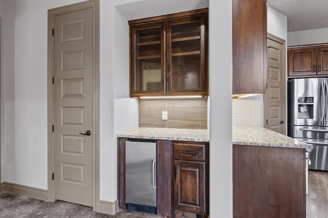 bar featuring light stone countertops, dark brown cabinets, tasteful backsplash, and stainless steel refrigerator with ice dispenser