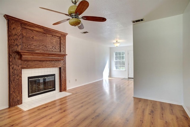 unfurnished living room with a textured ceiling, light wood-type flooring, a tile fireplace, and visible vents