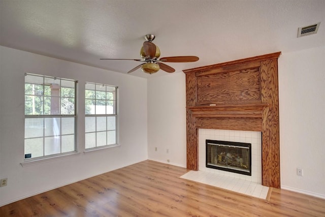 unfurnished living room featuring a ceiling fan, visible vents, a fireplace, and light wood-style flooring